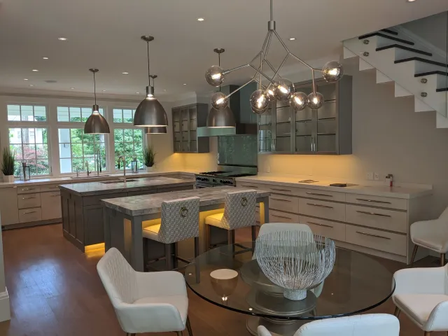 Modern kitchen with large window, island with marble countertop, pendant lights, glass-front cabinets, and a round dining table with white chairs.