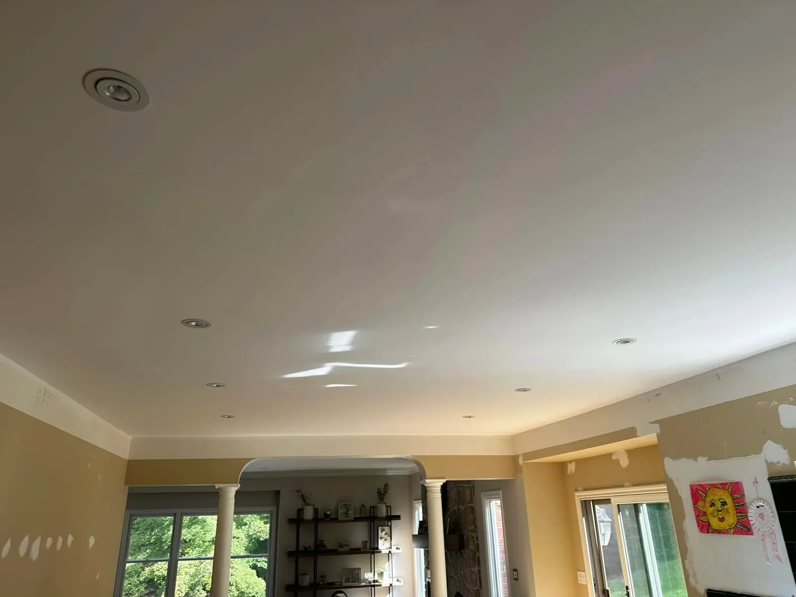 Living room with a freshly painted ceiling and walls, with large windows showing greenery outside.