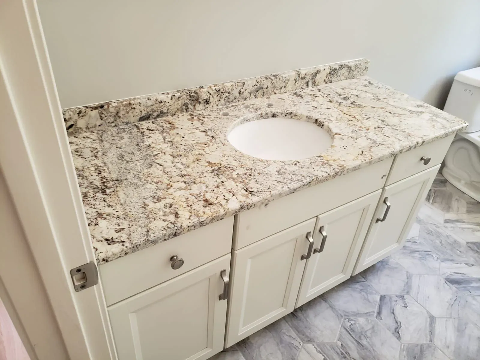 White vanity with granite countertop and built-in sink; a bathroom.
