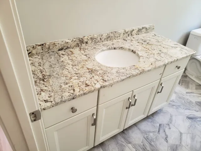 White vanity with granite countertop and built-in sink; a bathroom.
