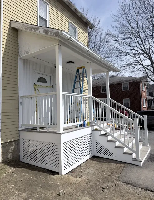 White porch with stairs and railing on a yellow house; ladder and blue bucket on the porch.