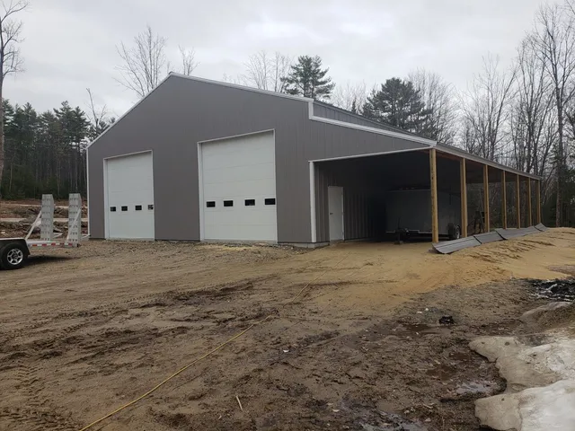 The same pole barn finished, with two overhead doors, grey steel siding and an open equipment bay along one side