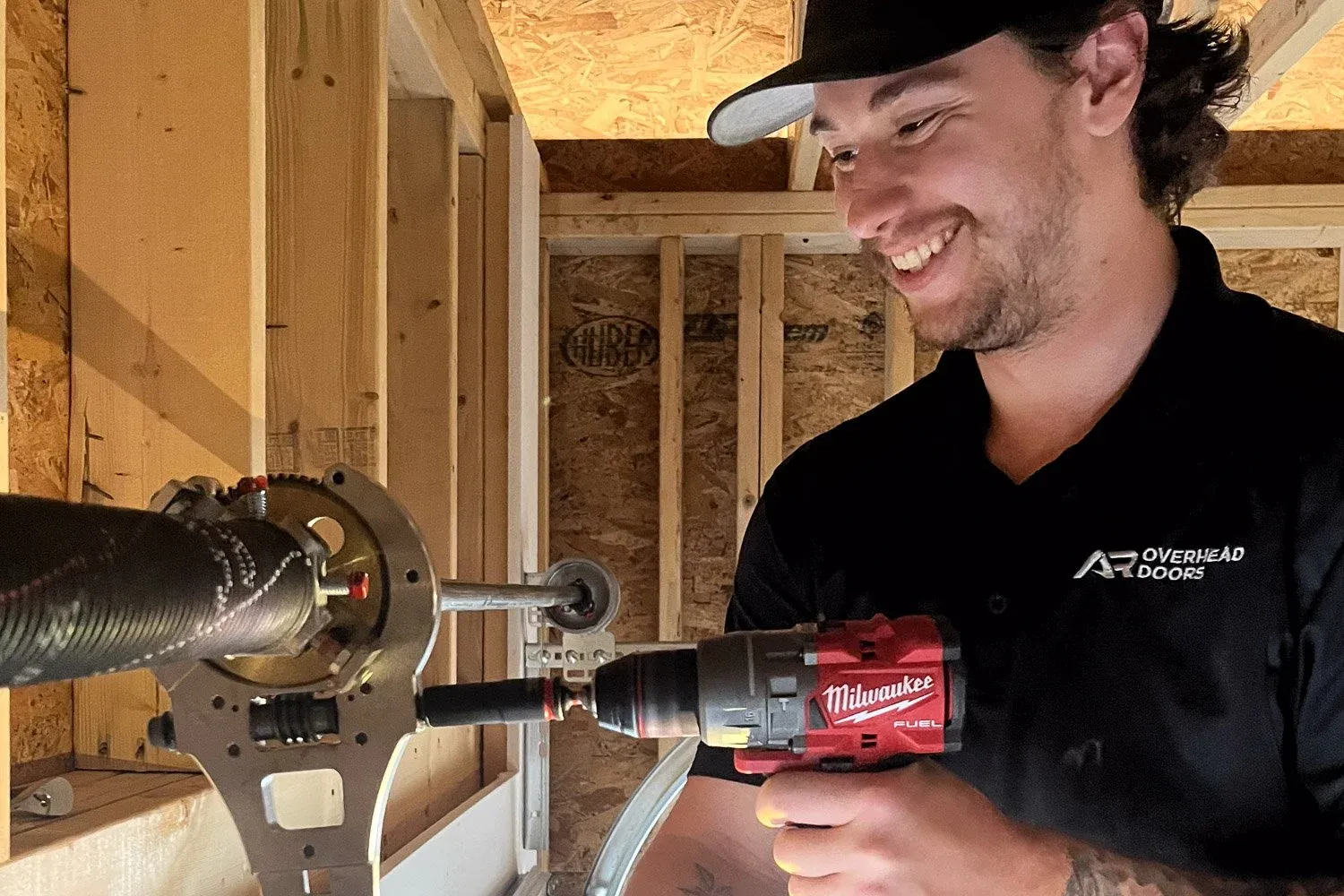 Man using a Milwaukee power drill to fix a garage door spring.