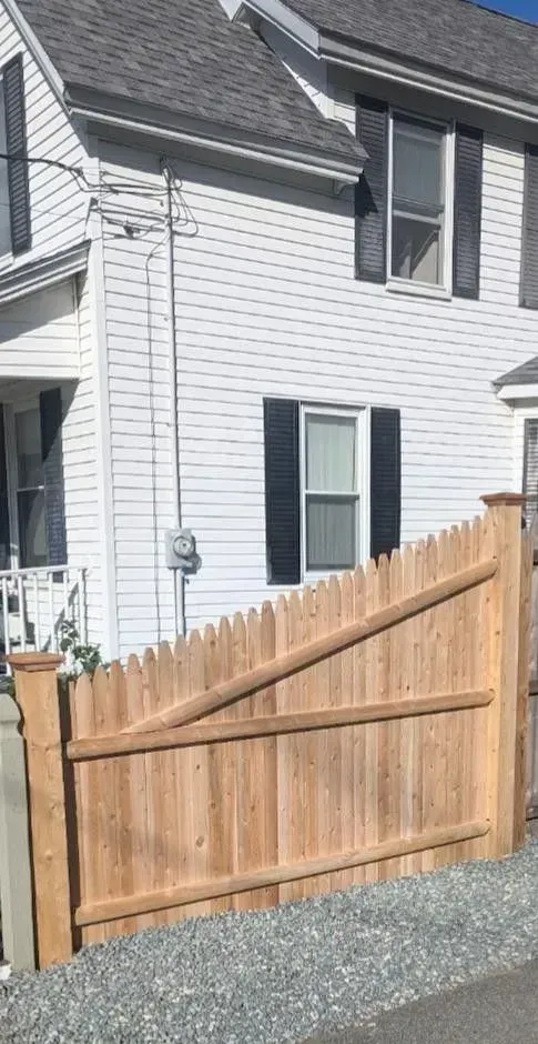 White house exterior with a wooden fence and gate beside a gravel driveway