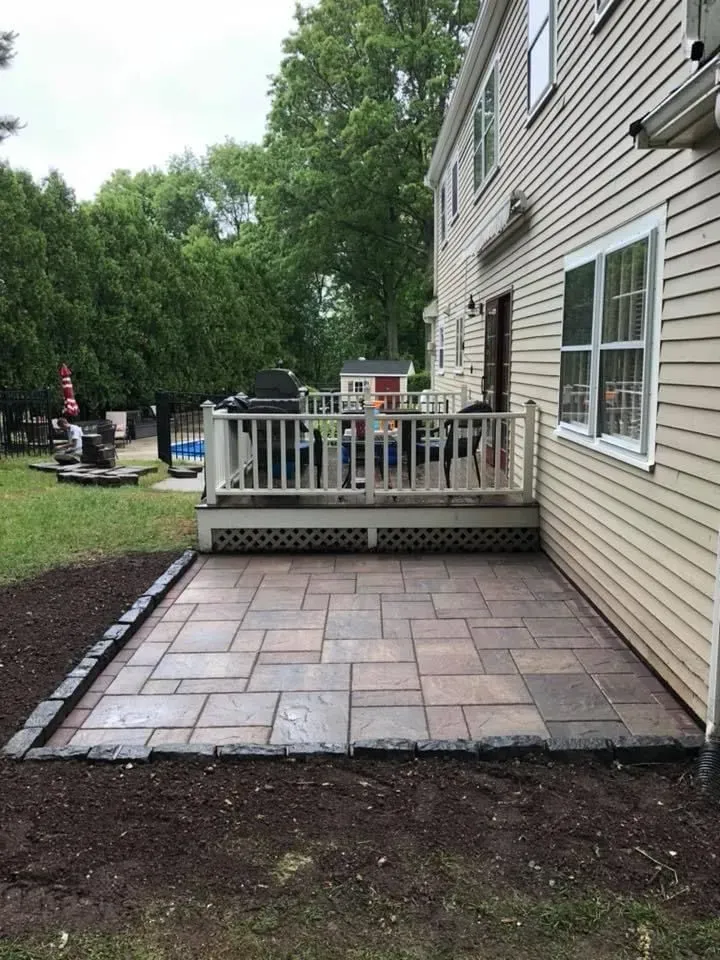 Backyard patio with stone pavers and a small wooden deck beside a beige house