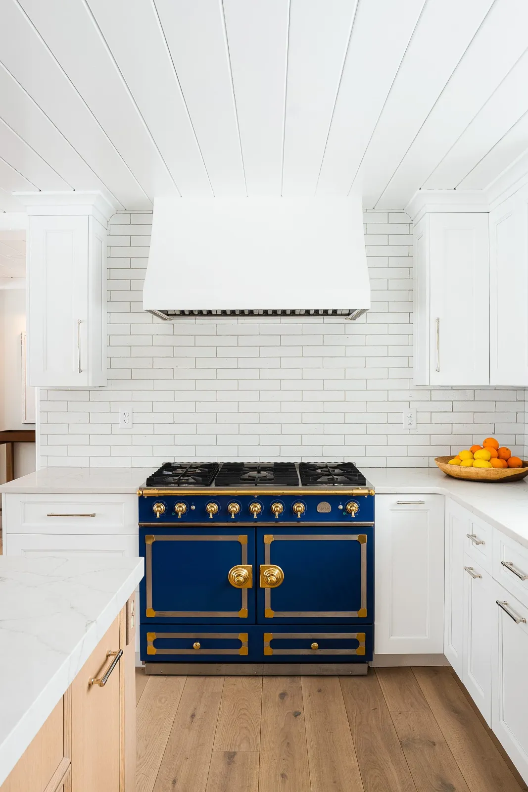 Hardwood floor installation in a Norwell kitchen with white cabinets, a white brick backsplash, a blue and gold stove, and a bowl of citrus fruits on the countertop.