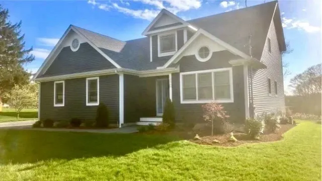 Modern dark gray house with white trim, large windows, and a well-maintained lawn under a blue sky.