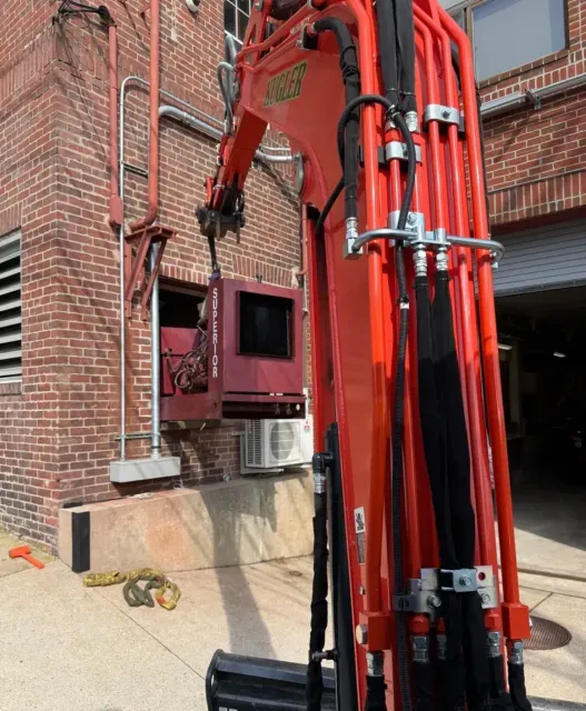 Red excavator arm working beside a brick building, with the cab near a basement window.