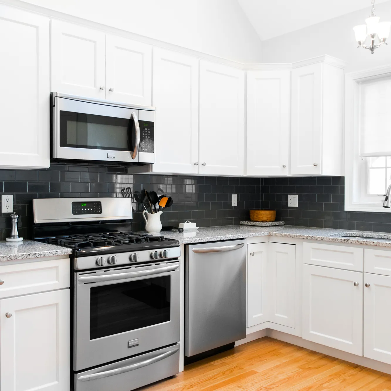 Modern kitchen with white cabinets, gray granite countertops, stainless steel appliances, and dark gray subway tile backsplash.