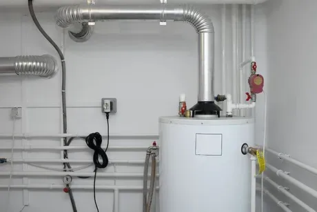 A water heater is sitting in a room next to pipes.