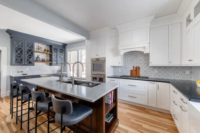 Modern white kitchen with island, black stools, mosaic backsplash, and stainless steel appliances