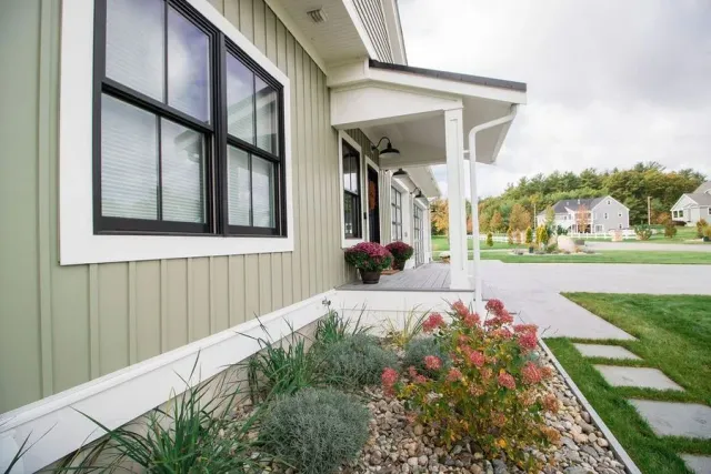Green house exterior with black window trim, porch, landscaping, and neighborhood view.