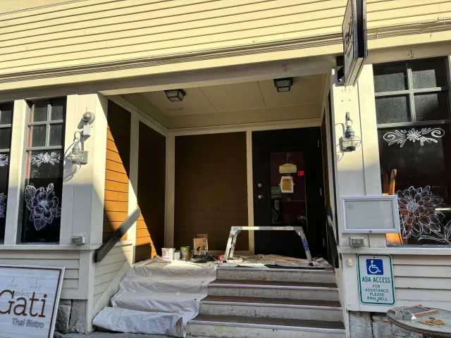 Exterior of a Thai bistro with entrance being painted, showing a closed door, paint supplies and a handicap access sign.
