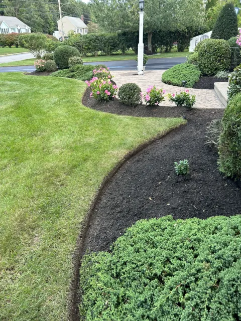 Curved mulch bed with shrubs and flowering plants installed in a residential front yard by A. Fowkes Landscape & Construction