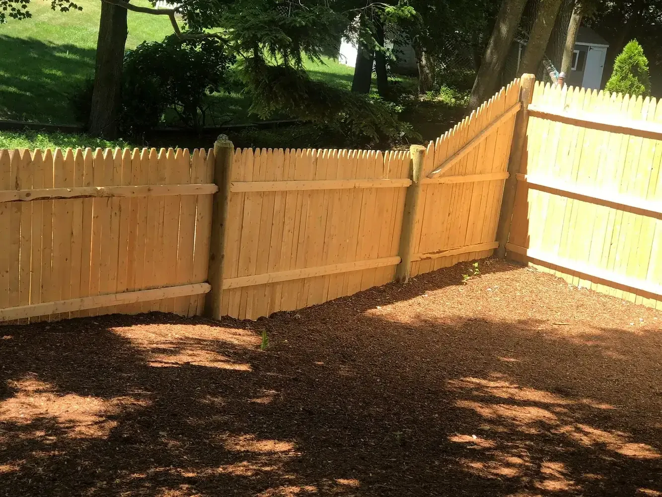 Newly installed wood stockade fence with fresh mulch bed