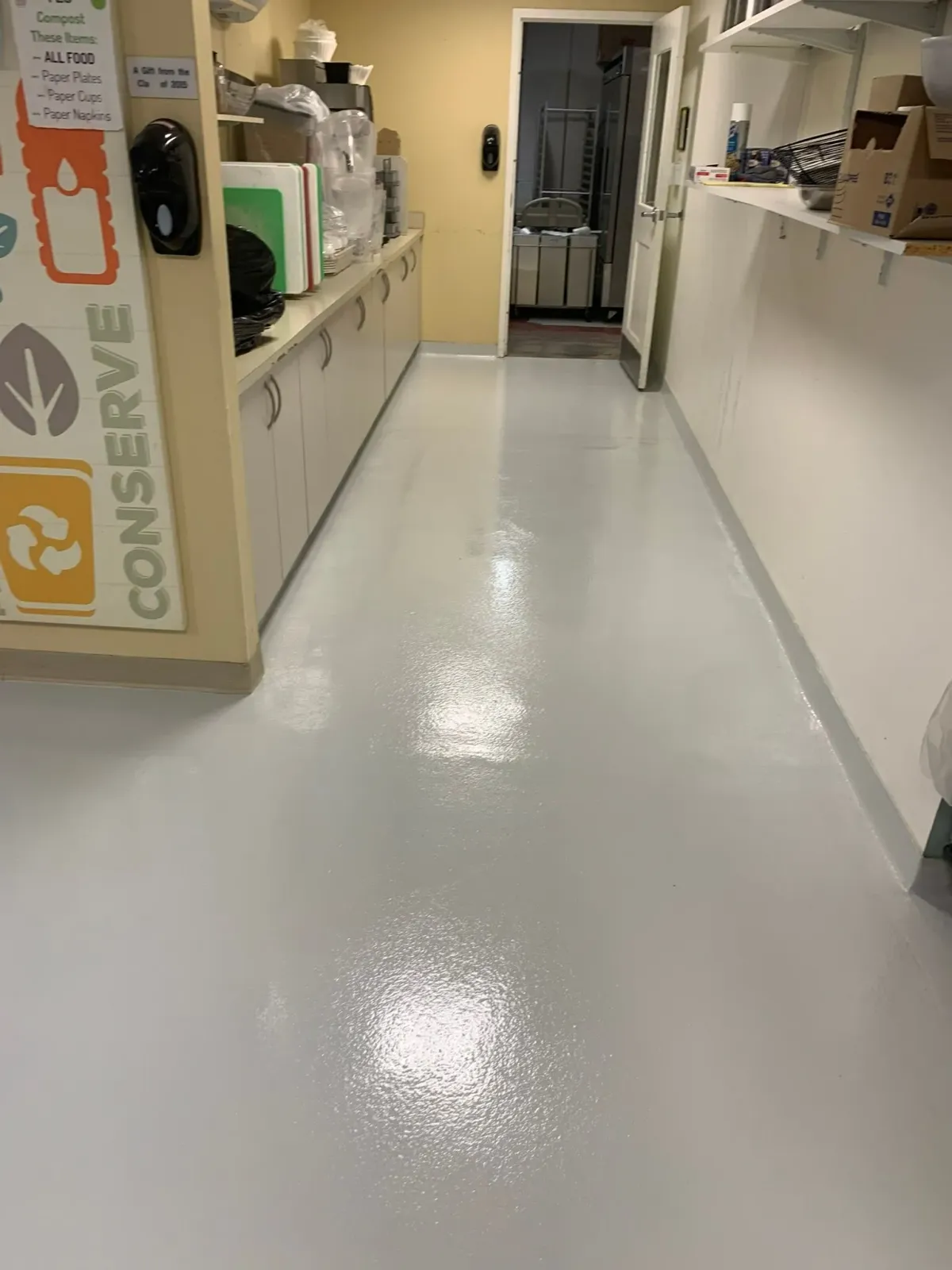 Shiny hospital corridor with white counters and a doorway at the end, viewed from the hallway.