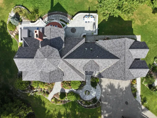 Large house with gray shingle roof and circular driveway from above