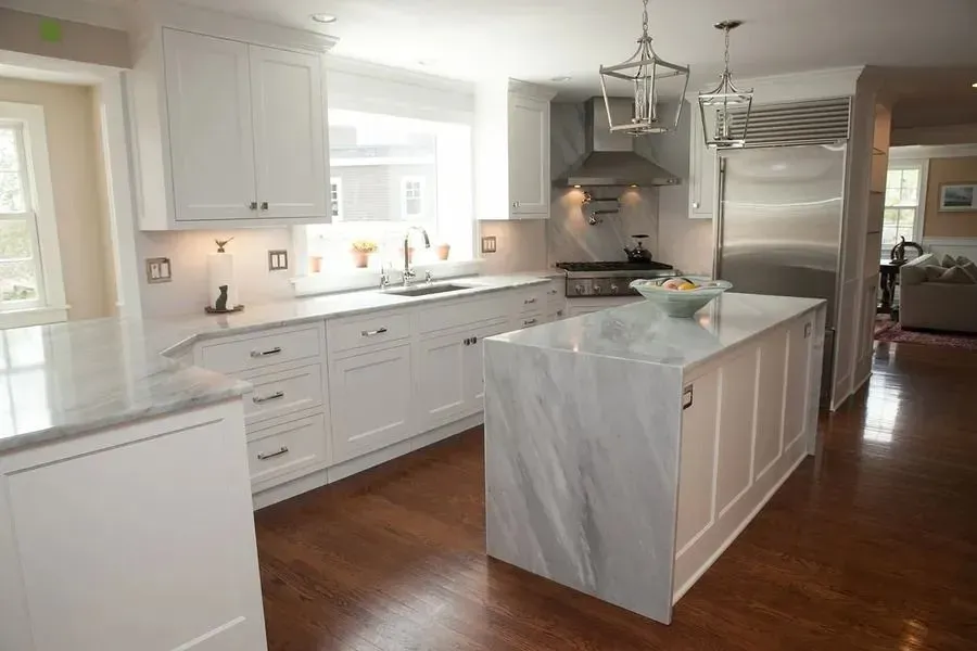 Bright modern kitchen with white cabinets, marble island, stainless steel appliances, and hardwood floors