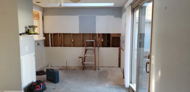 Kitchen under renovation, walls partially stripped, exposed studs. Step ladder in