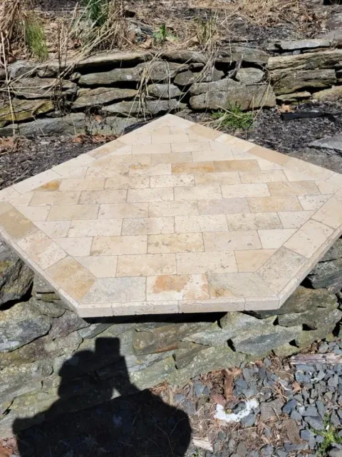 Beige hexagonal stone patio or table base on a rocky ground, with a stone wall behind.