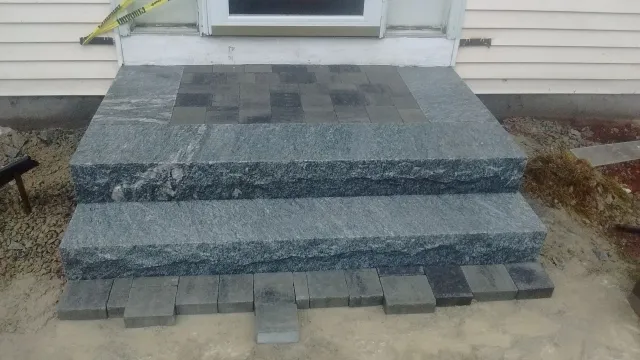 Newly installed granite steps and a paver landing in Webster, MA, in front of a house entrance, with caution tape indicating ongoing construction. Project by KRD Landscaping.