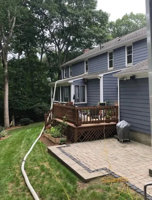 A backyard with a blue house, getting blown-in insulation services by NetZero Insulation Technologies crew.
