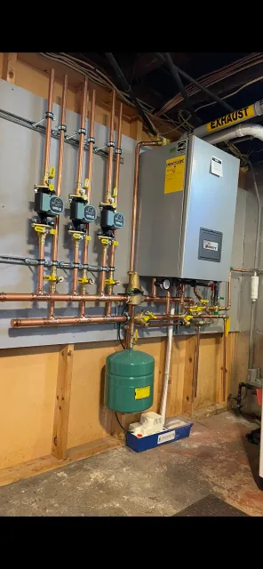 Basement with boiler, copper pipes, pressure gauges, green expansion tank, and exhaust duct.