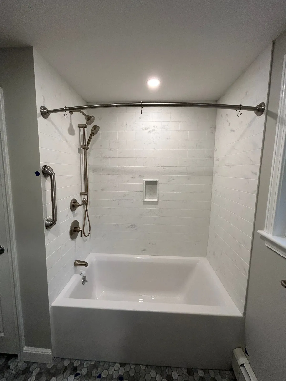 Bathroom with white bathtub, shower curtain rod, handheld shower, and grab bars in a tiled alcove.