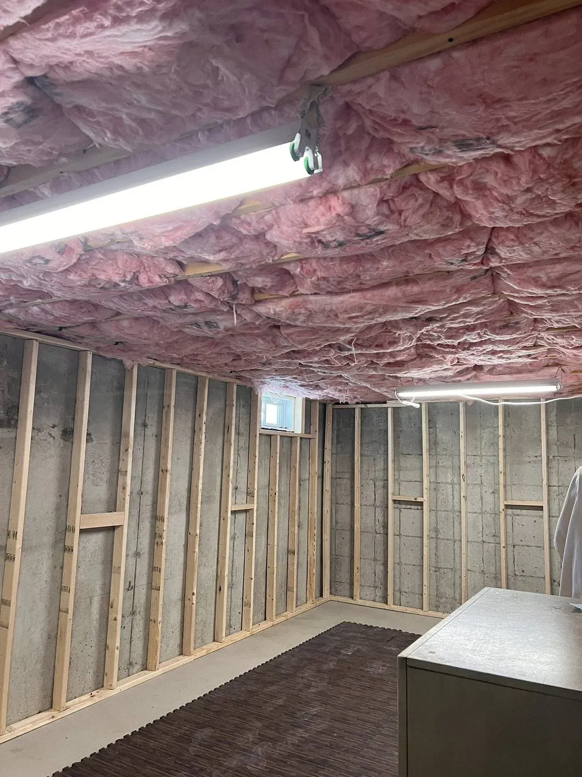 Basement framing with pink fiberglass insulation in ceiling joists and new stud walls along concrete