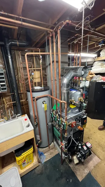 Mechanical room with exposed copper pipes, boiler equipment, and utility tanks in a basement.