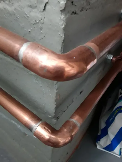 Close-up of copper pipes against a concrete wall.