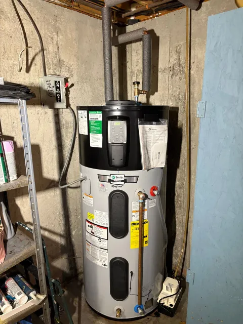 A water heater in a basement setting with insulated pipes and wall.