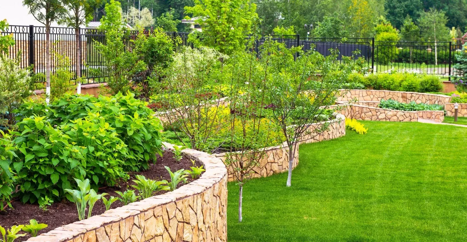 Curved stone garden beds with lush green plants and a manicured lawn in a bright landscaped yard