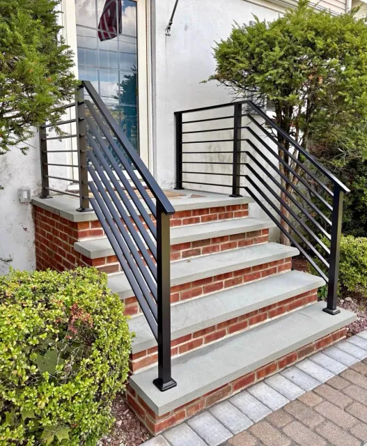 Front steps with black railings leading to a house entrance, bordered by brick and brick pavers