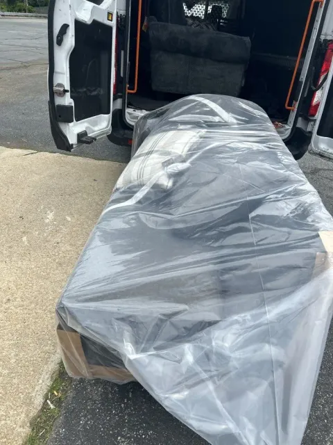 A sofa wrapped in plastic is being loaded into a white cargo van.