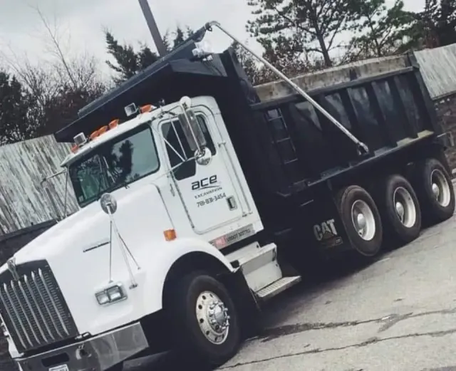 White dump truck parked at an angle on a paved lot, black bed raised slightly.