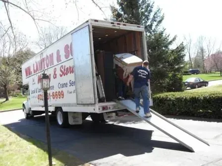 Movers loading furniture into a white moving truck parked on a driveway.