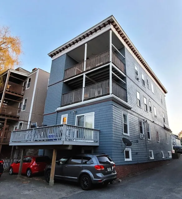 Home Association owned three-story blue apartment building with balconies, parking underneath, and several parked cars in front freshly painted.