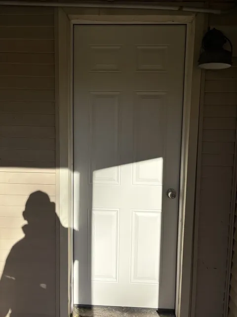 After replacement: newly installed white six-panel exterior door closed in the finished doorway