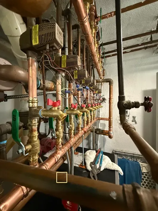 Copper industrial piping and valves in a mechanical room, with gauges and insulated pipes overhead.