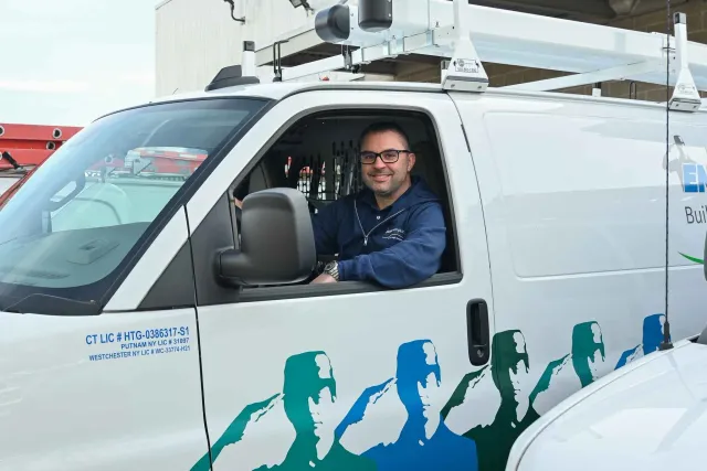 A man sitting in the driver's seat of a white Encon Heating & AC utility truck, smiling at the camera.