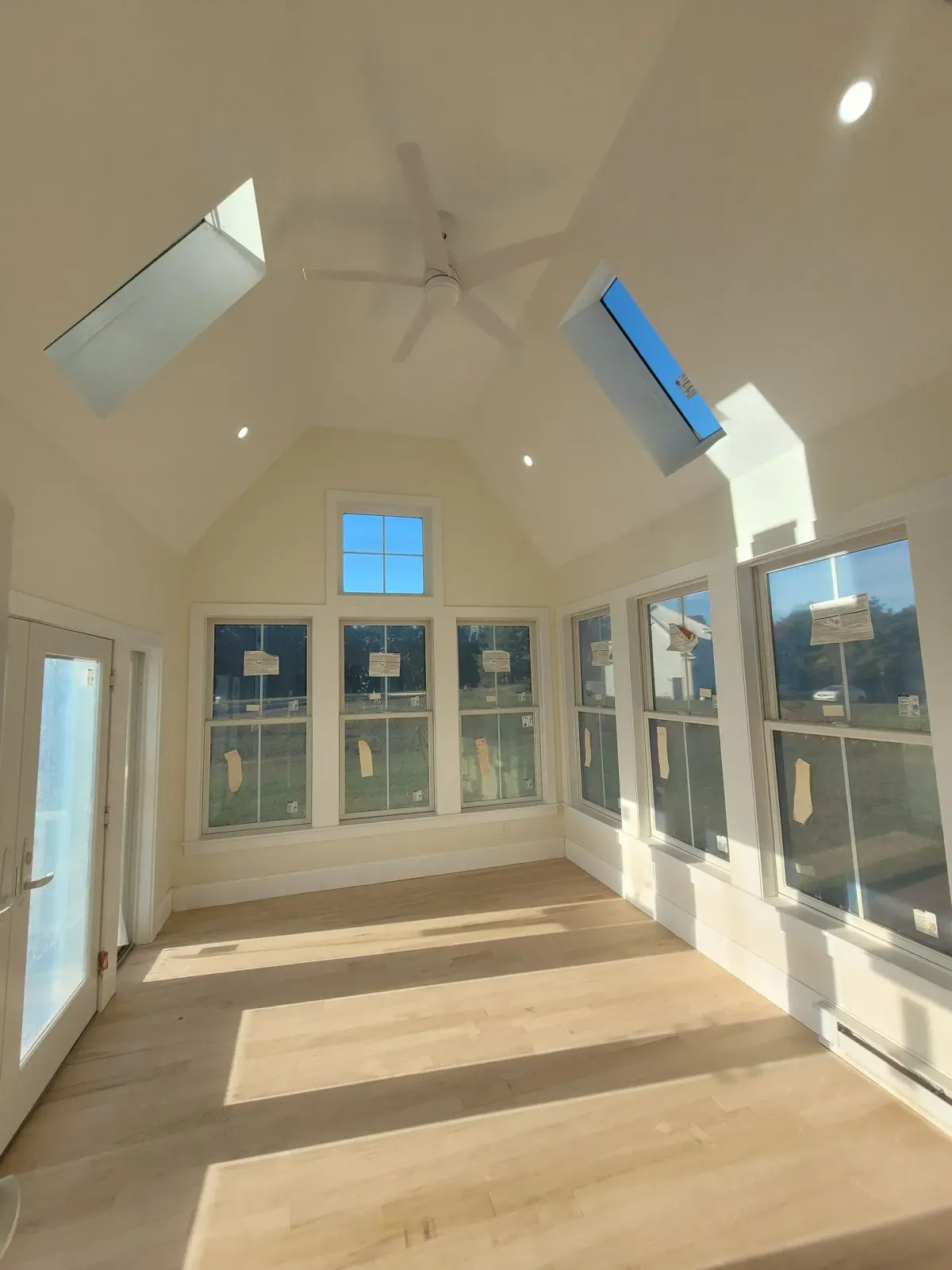 Bright, white sunroom interior with skylights, multiple windows, light wood floor, and a ceiling fan.