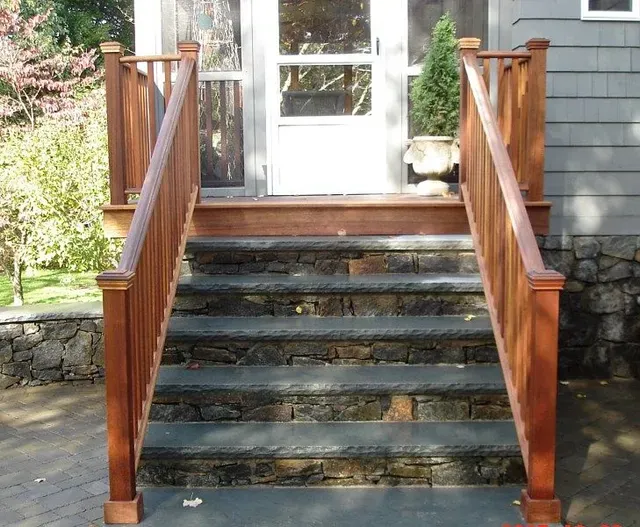 Front porch with stone steps and wooden railings leading to a white door