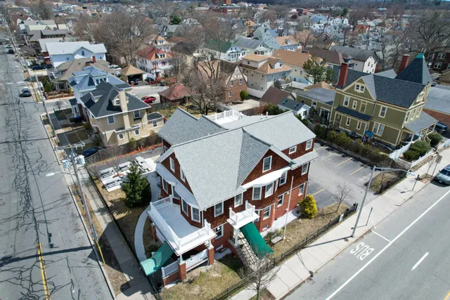 Aerial view of a three-story home with a new gray shingle roof on a city street
