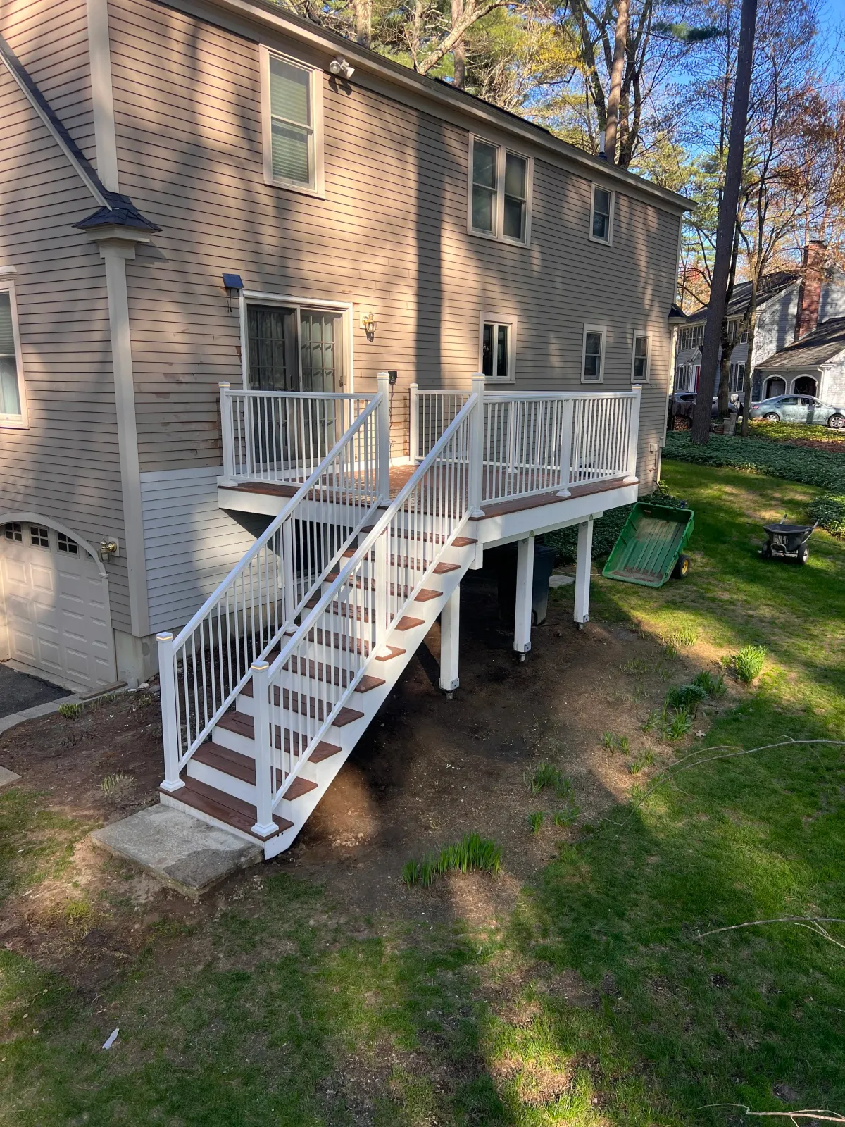 View of a backyard deck with a railing, looking out onto a grassy yard with trees, a children's playset, a trampoline, and outdoor equipment.