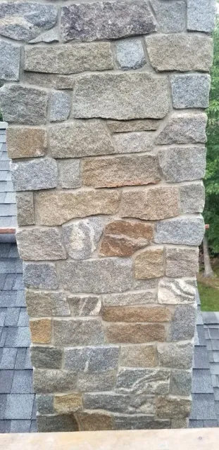Close-up of a stone chimney on a house, showing variously shaped and colored stones with mortar.