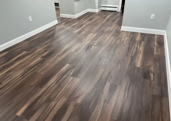 Dark wood-look flooring with white baseboards and gray walls in an empty room.