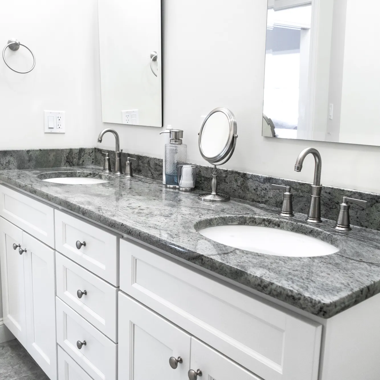 Double sink vanity with white cabinets and a gray stone countertop.