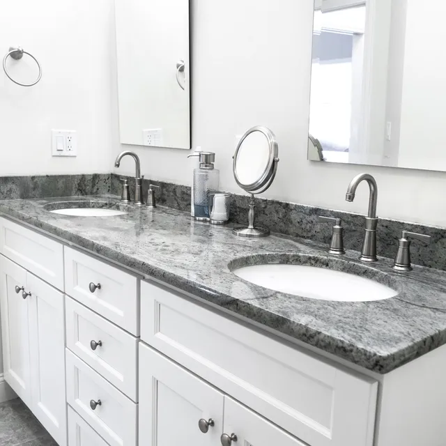 Double sink vanity with white cabinets and a gray stone countertop.