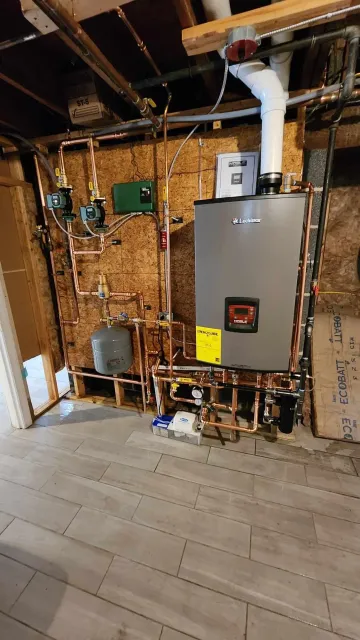 A home's utility room with a Lochinvar hot water heater, copper piping, gauges, and other plumbing components installed on a wooden wall.